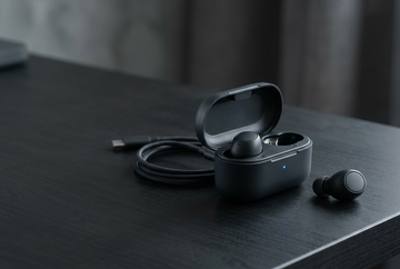 Wireless earbuds and charging case on a dark desk with subtle blue lighting
