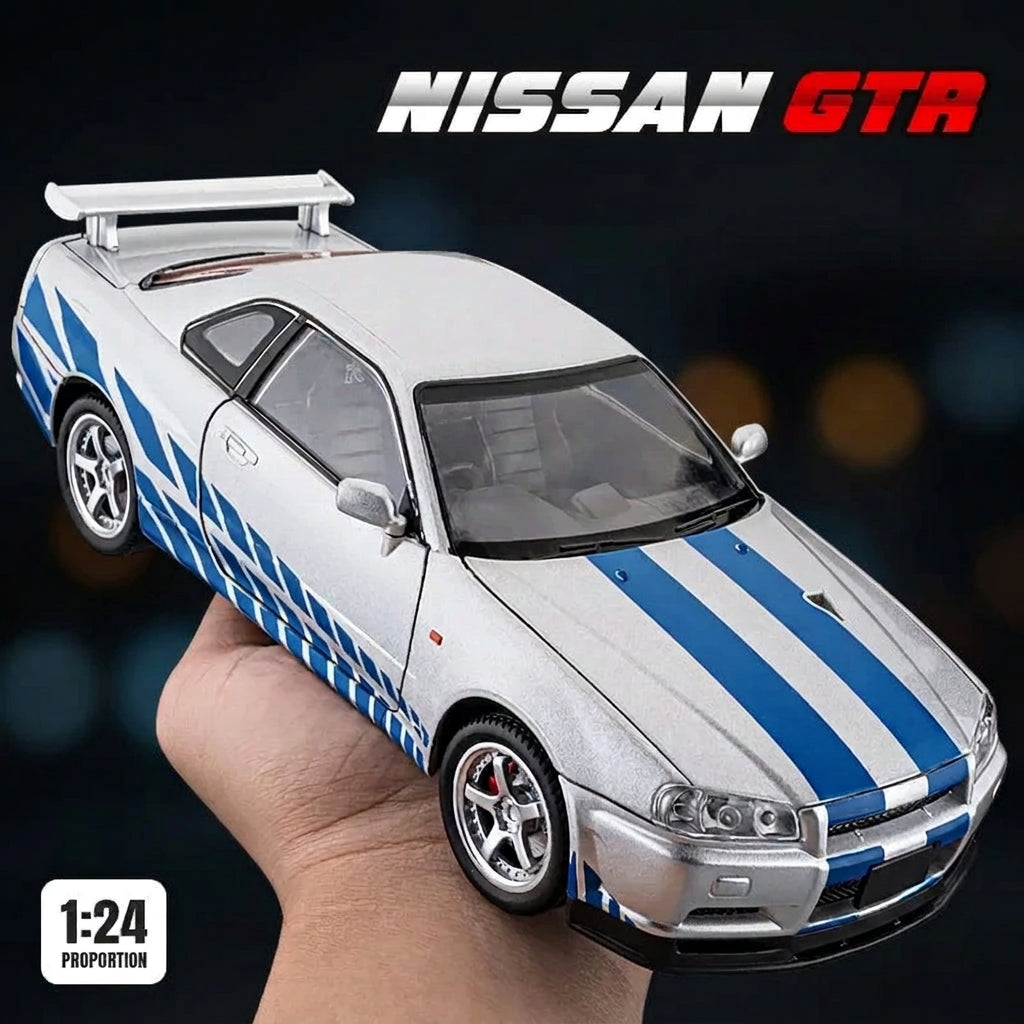 A 1:24 scale model of a silver Nissan GTR with blue racing stripes, held in a hand against a dark gray background